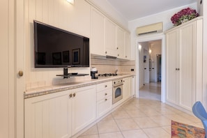 A modern kitchen with white cabinetry, a built-in stove, and a large flat-screen TV mounted above the counter. - Palm House apartment in elegant, central setting, a few steps from the sea. (Bordighera)