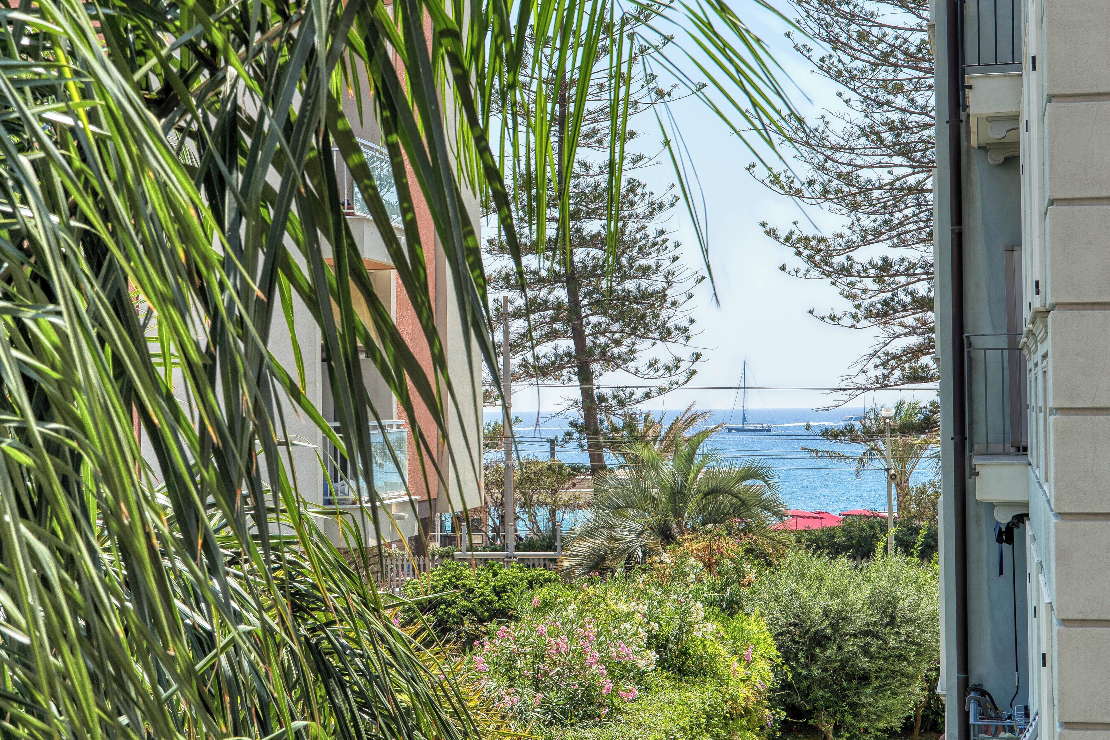 A view of a coastal area with a building, greenery, and a bridge in the distance.