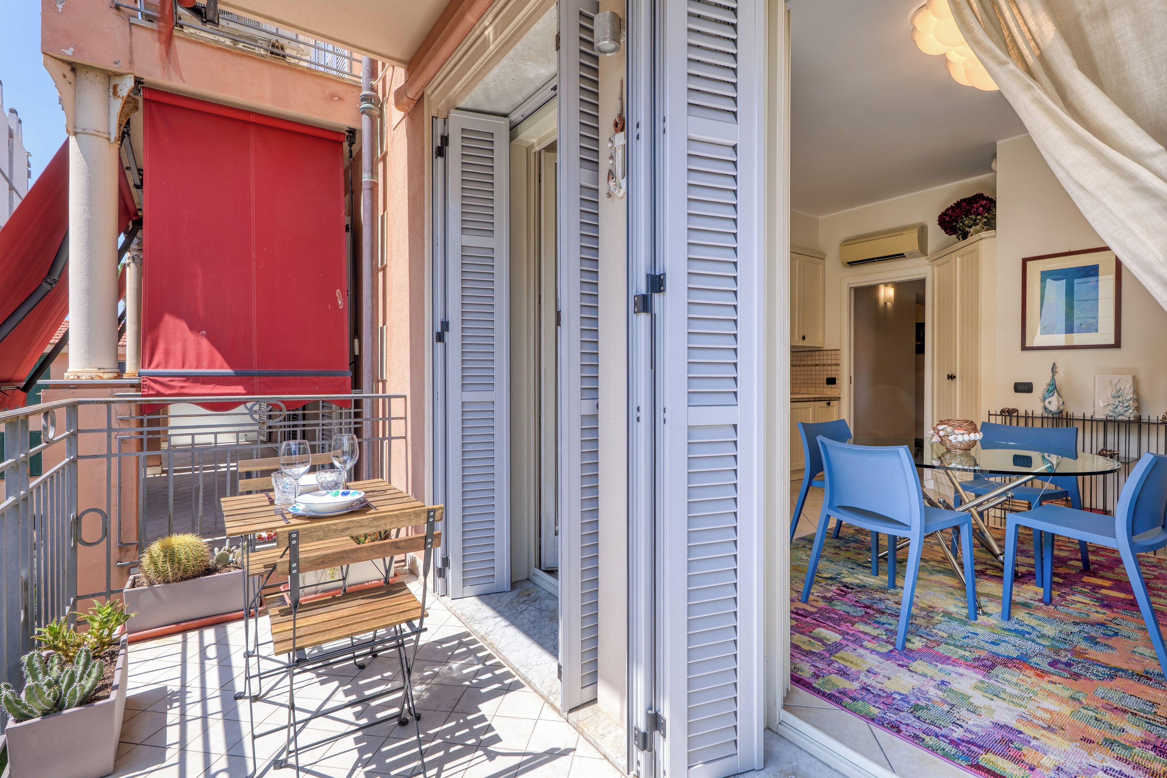 Un balcon avec un auvent rouge, une table avec des chaises et un tapis coloré à l’intérieur d’une pièce.