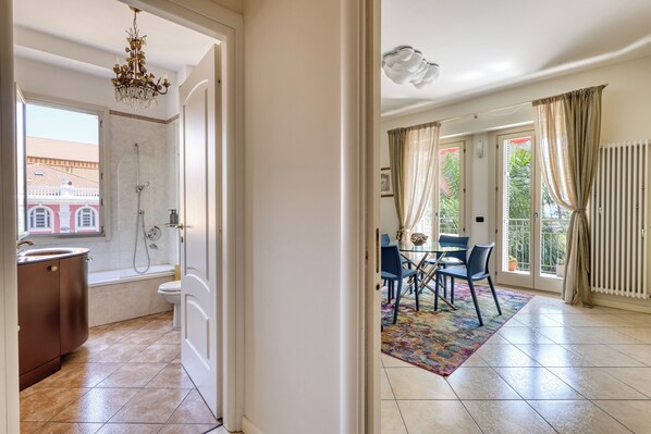 A hotel room with a bathroom, a dining area with a table and chairs, and a view of the outside. - Palm House Apartment in an elegant, central setting, just a few steps from the ocean. (Bordighera)