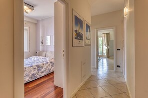 A hallway leading to a bedroom with a bed, framed pictures on the walls, and a view of the outdoors through a door. - Palm House Apartment in an elegant, central setting, just a few steps from the ocean. (Bordighera)