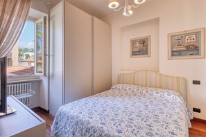 A bedroom with a bed, a window with curtains, a radiator, and two framed pictures on the wall.