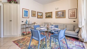 Een eetgedeelte met een glazen tafel, blauwe stoelen en een kleurrijk vloerkleed.