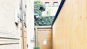 Un estrecho callejón con una verja de madera, plantas en macetas y un edificio con tejado de tejas al fondo.