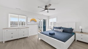 Ein Schlafzimmer mit Bett, Deckenventilator, Kommode, Nachttisch und einem Fenster mit Jalousien.