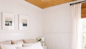 Una camera da letto con soffitto in legno, un letto grande con lenzuola bianche, un comodino con una lampada e due quadri appesi al muro.