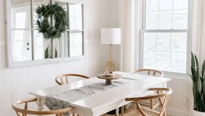 Una sala da pranzo con un tavolo bianco, quattro sedie di legno, un soffitto in legno, una finestra con vista e una pianta in vaso.