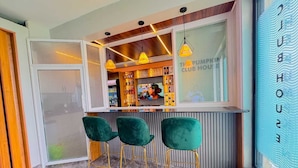 Zona de bar con tres taburetes de terciopelo verde, una barra y un barman.
