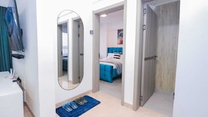 Una habitación de hotel moderna con un espejo grande, una cama con ropa de cama azul, una alfombra azul y una puerta de madera.
