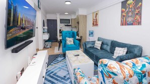 Una sala de estar moderna con un televisor de pantalla plana, un sofá azul, un sillón estampado y una mesa de centro.