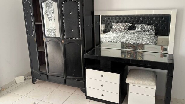 Ein Schlafzimmer mit einem schwarzen Kleiderschrank, einem Schminktisch mit Spiegel und einem Bett mit einer gesteppten Kopfteil.