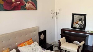 Ein Schlafzimmer mit Bett, Schreibtisch, Stuhl, Stehlampe und einem Bild an der Wand.