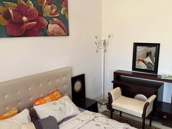 A bedroom with a bed, a desk, a chair, a floor lamp, and a painting on the wall.