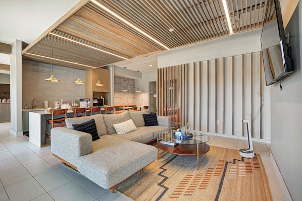 A modern living room with a sectional sofa, a glass coffee table, and a kitchen in the background.
