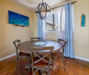 Un coin repas comprenant une table ronde en bois, quatre chaises, un lustre, un tableau et une fenêtre avec des rideaux.