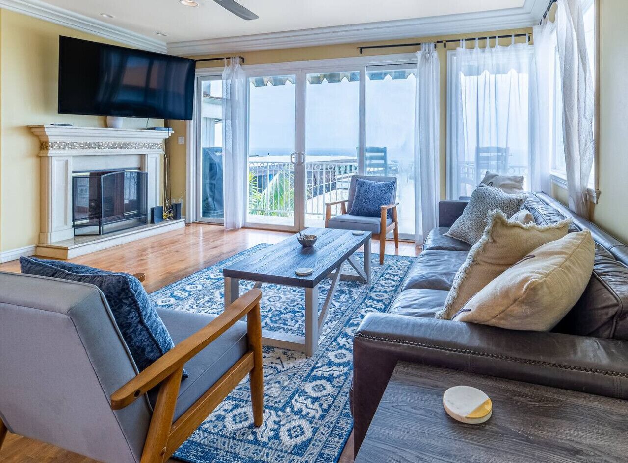 A spacious living room with a fireplace, a large TV, a sofa, and a balcony with a view.