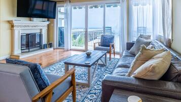 A spacious living room with a fireplace, a large TV, a sofa, and a balcony with a view.
