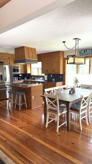 A kitchen with wooden cabinets, a central island, and a dining area with white chairs. - LAKE DAZE 4-bedroom Lakefront home in quiet cove on Pea Hill Creek (Henrico)