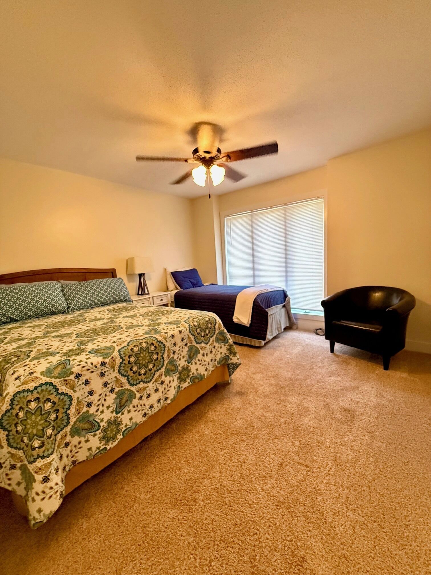 A bedroom with a bed, a chair, a ceiling fan, and a window with blinds.