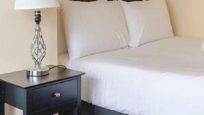 Una habitación de hotel con cama, mesita de noche con lámpara y cabecero oscuro.