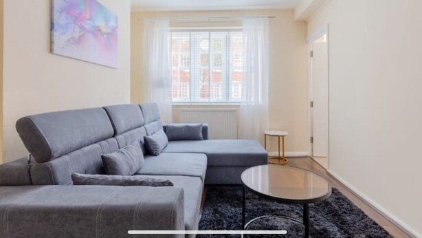 Una sala de estar moderna con un sofá modular gris, una mesa de centro redonda de vidrio y un cuadro abstracto colorido en la pared.