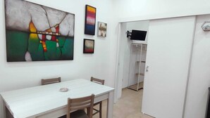 A dining area with a white table and chairs, a painting on the wall, and a television mounted on the wall. - Angy's Little House is a small abode a 10-minute walk from downtown (Palermo)