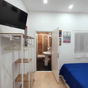 A bedroom with a bed, a wardrobe, a television, and a bathroom visible through an open door. - A small house in Angy, a 10-minute walk from downtown (Palermo)