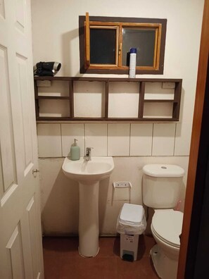 Ein kleines Badezimmer mit einem Standwaschbecken, einer Toilette und einem Regal über dem Waschbecken.