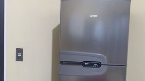 Frigorifero in acciaio inox con display digitale, posizionato di fronte a una parete liscia con pavimento piastrellato.