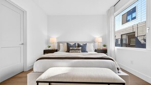 Un dormitorio moderno con una cama grande, mesitas de noche con lámparas, un banco y vistas del exterior.