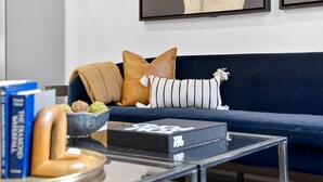 Una sala de estar moderna con un sof á azul oscuro, una mesa de centro de vidrio y un tazón de bocadillos.