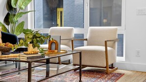 Una sala de estar moderna con un ventanal grande, dos sillones, una mesita de centro y una planta en maceta.