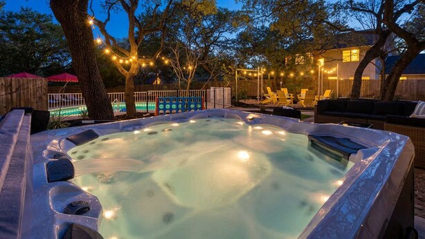Een hottub omringd door bomen, een houten terras en lichtjes.