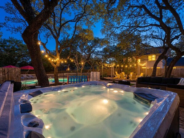 Ein Whirlpool, umgeben von Bäumen, einer Holzterrasse und Lichterketten.