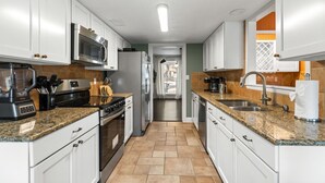 Een moderne keuken met witte kasten, granieten aanrechtbladen, roestvrijstalen apparatuur en een doorkijk.