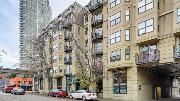 Un immeuble résidentiel à plusieurs étages, doté de balcons, d’une entrée de garage et de voitures garées dans la rue.