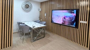 Una zona menjador moderna amb una paret de panells de fusta, un rellotge rodó de paret i un televisor de pantalla plana encastat a la paret.