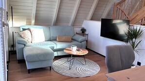 A loft-style living room with a light blue sofa, a round coffee table, and a television mounted on the wall. - Chalet on the Biggesee (Olpe)