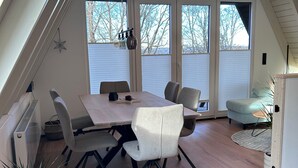 A modern dining area with a wooden table and chairs, large windows, and a view of trees. - Chalet on the Biggesee (Olpe)