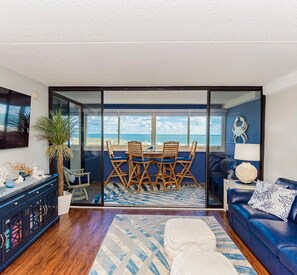 Un soggiorno con vista sull'oceano, una zona pranzo con sedie di legno, un divano blu e un mobile decorativo.