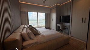 Quarto moderno com uma cama grande, área de estar, televisão e vista para o mar.