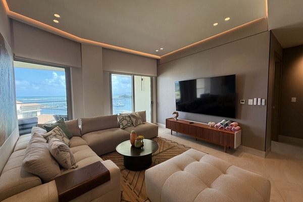 Comfortable living room with large sectional sofa, smart 86` TV, and access to balcony with marina views.
