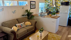 Una sala de estar acogedora con un sofá, una mesa de centro y una zona de cocina con refrigerador, microondas y pileta.