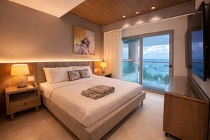 A hotel room with a large bed, a television, a balcony with a view, and a painting on the wall.