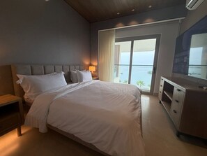 Ein Hotelzimmer mit einem großen Bett, einem Nachttisch, einer Kommode und Meerblick durch ein großes Fenster.