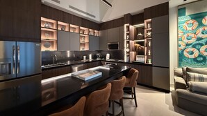 A modern kitchen with a central island, bar stools, built-in shelving, and a dining area with a sofa.