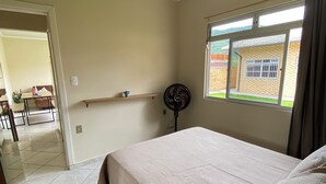 Et soveværelse med en seng, en ventilator, et vindue og udsigt til et hus.