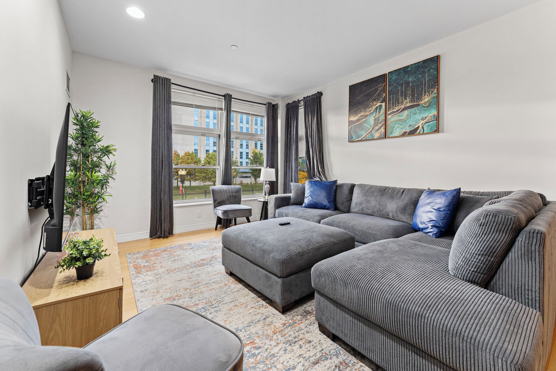 A modern living room with a grey sectional sofa, a small table, and a TV mounted on the wall.