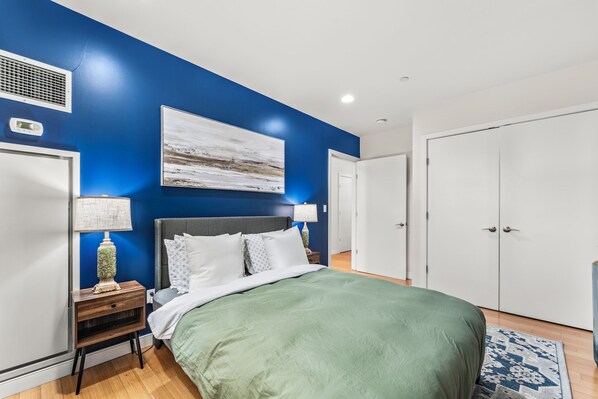 A bedroom with a bed, nightstands, a lamp, a painting, and a wardrobe. - Furnished Apartment near BMC (Boston)
