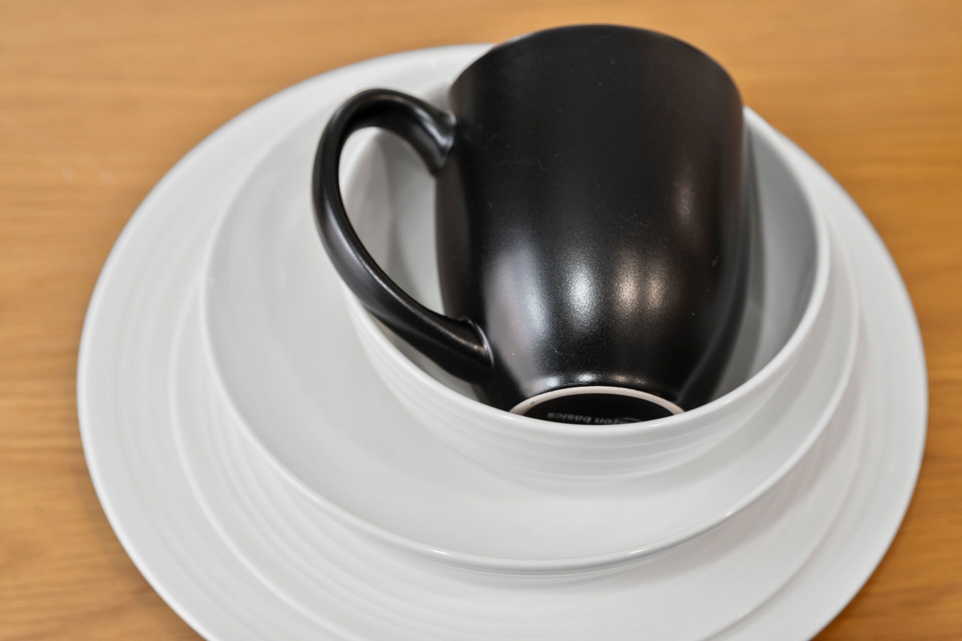 En sort kop på en hvid underkop og tallerken placeret på et træbord.